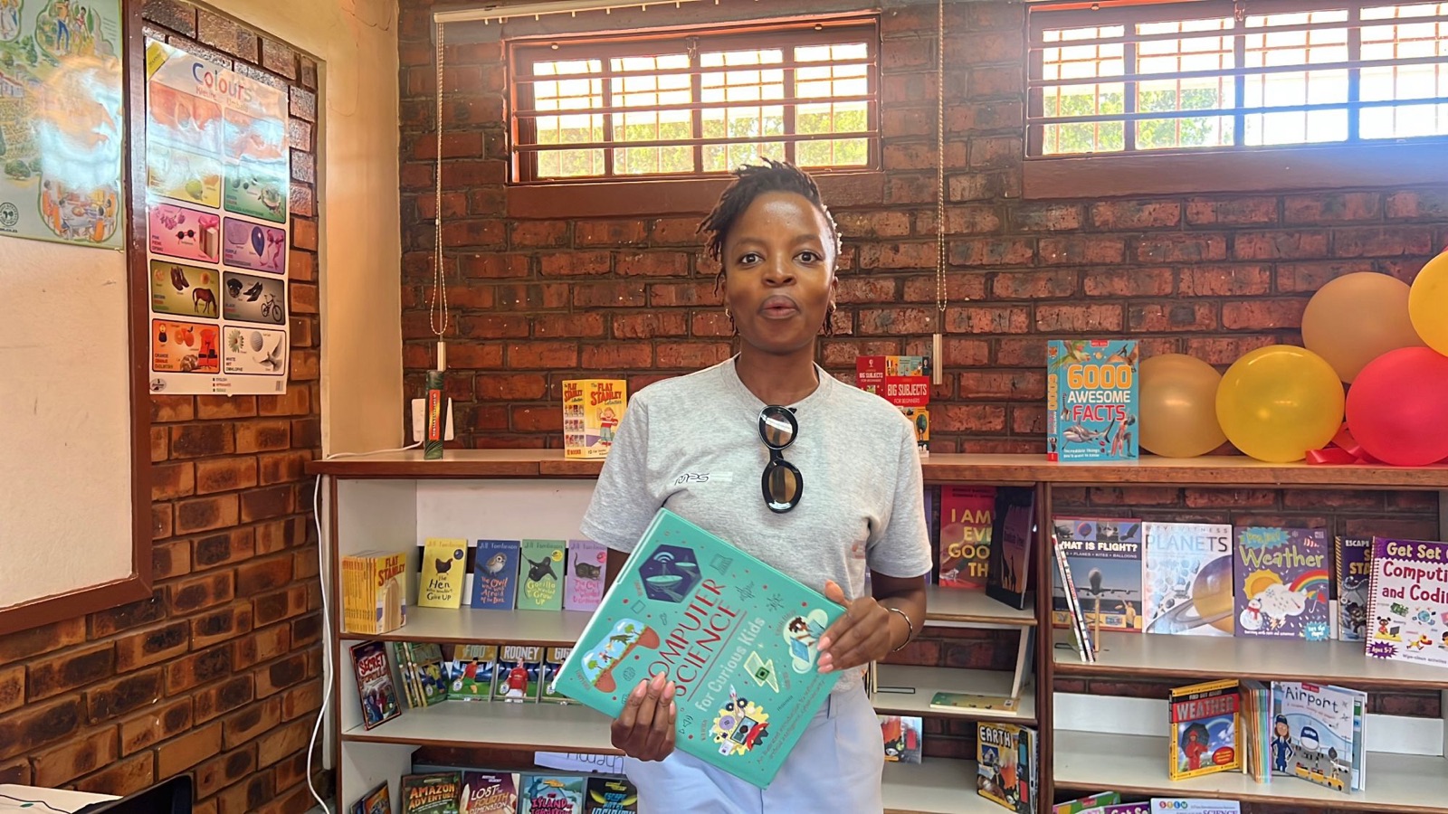 Nthabiseng Makhoba holds up Computer Science for Curious Kids in front of the library's new bookshelves