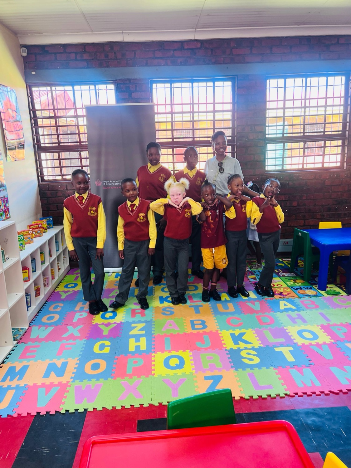 Learners pose playfully on the alphabet mat in the new library corner with Nthabiseng
